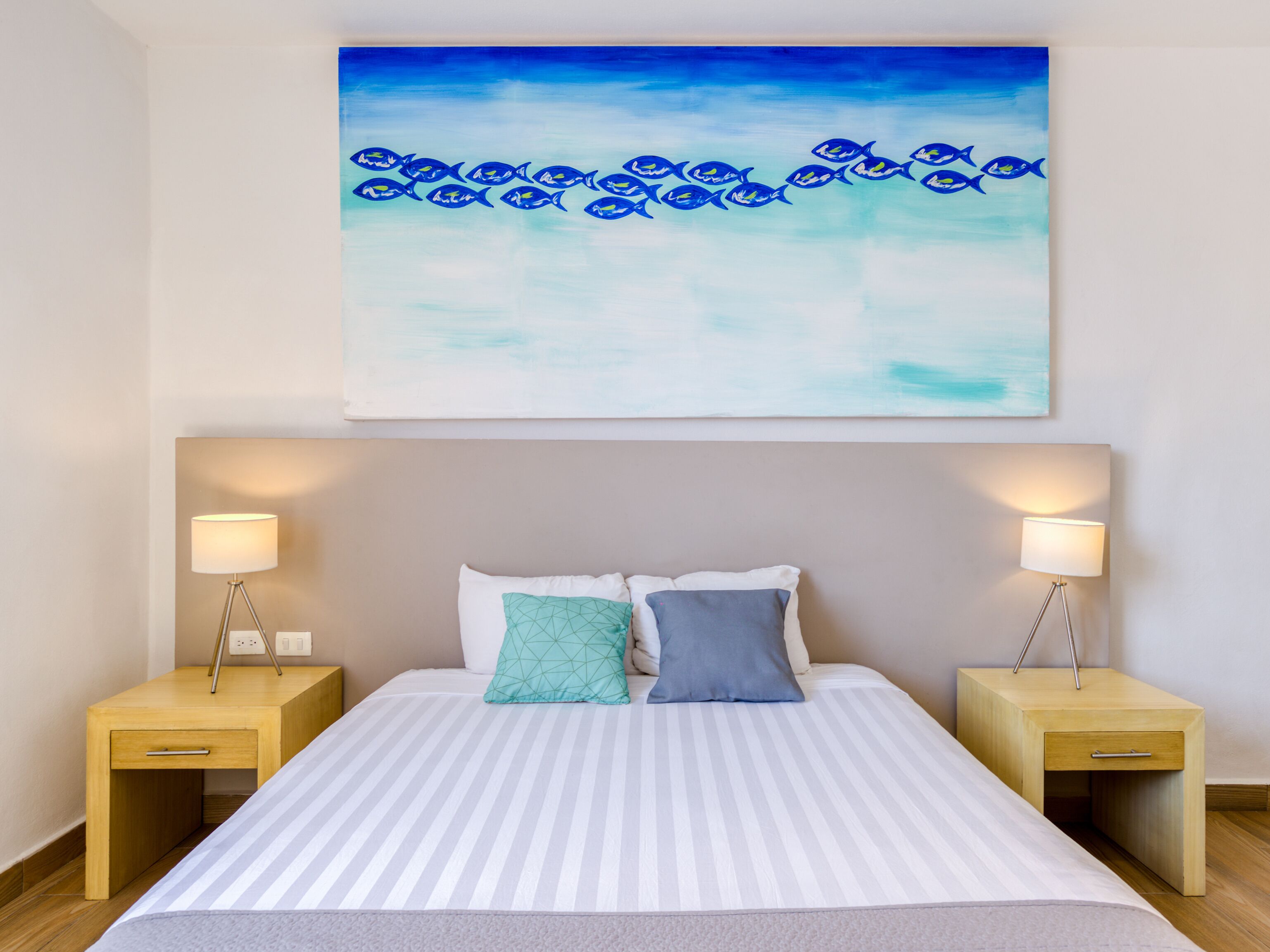 Une chambre d’hôtel avec un lit, deux tables de chevet et un tableau représentant des poissons au mur.