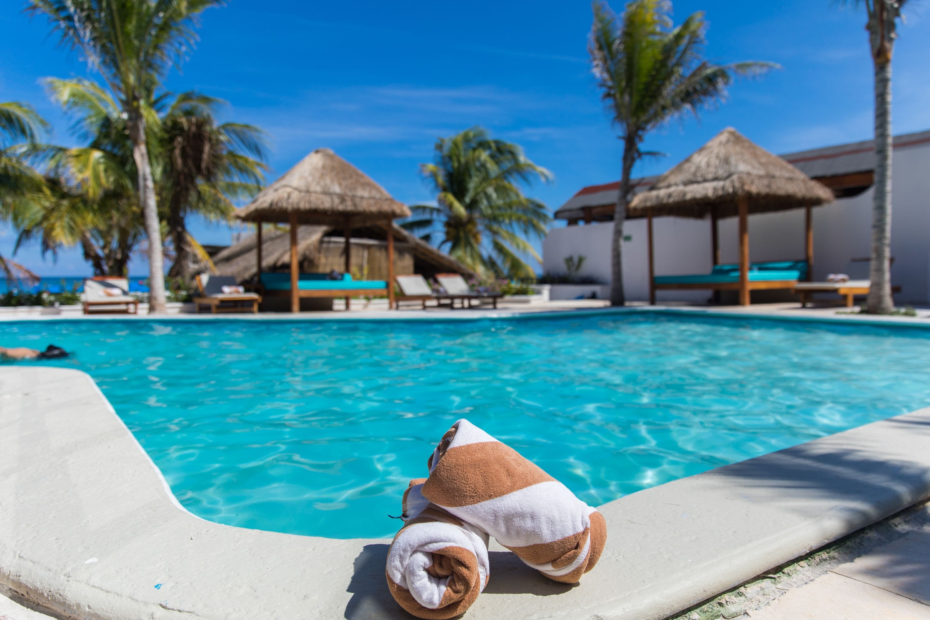 Une piscine entourée de palmiers, avec des chaises longues et des parasols en feuilles de palmier.