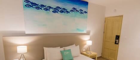 A modern hotel room with a large bed, two bedside tables with lamps, a wooden floor, and a painting above the bed.