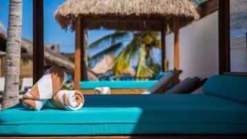 A beachside lounge with a thatched roof, turquoise lounge chairs, and a palm tree in the background.