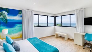 A modern hotel room with a large bed, a desk, a chair, and a TV. The room has large windows with a view of the ocean. - Hotel Ojo de Agua (Puerto Morelos)
