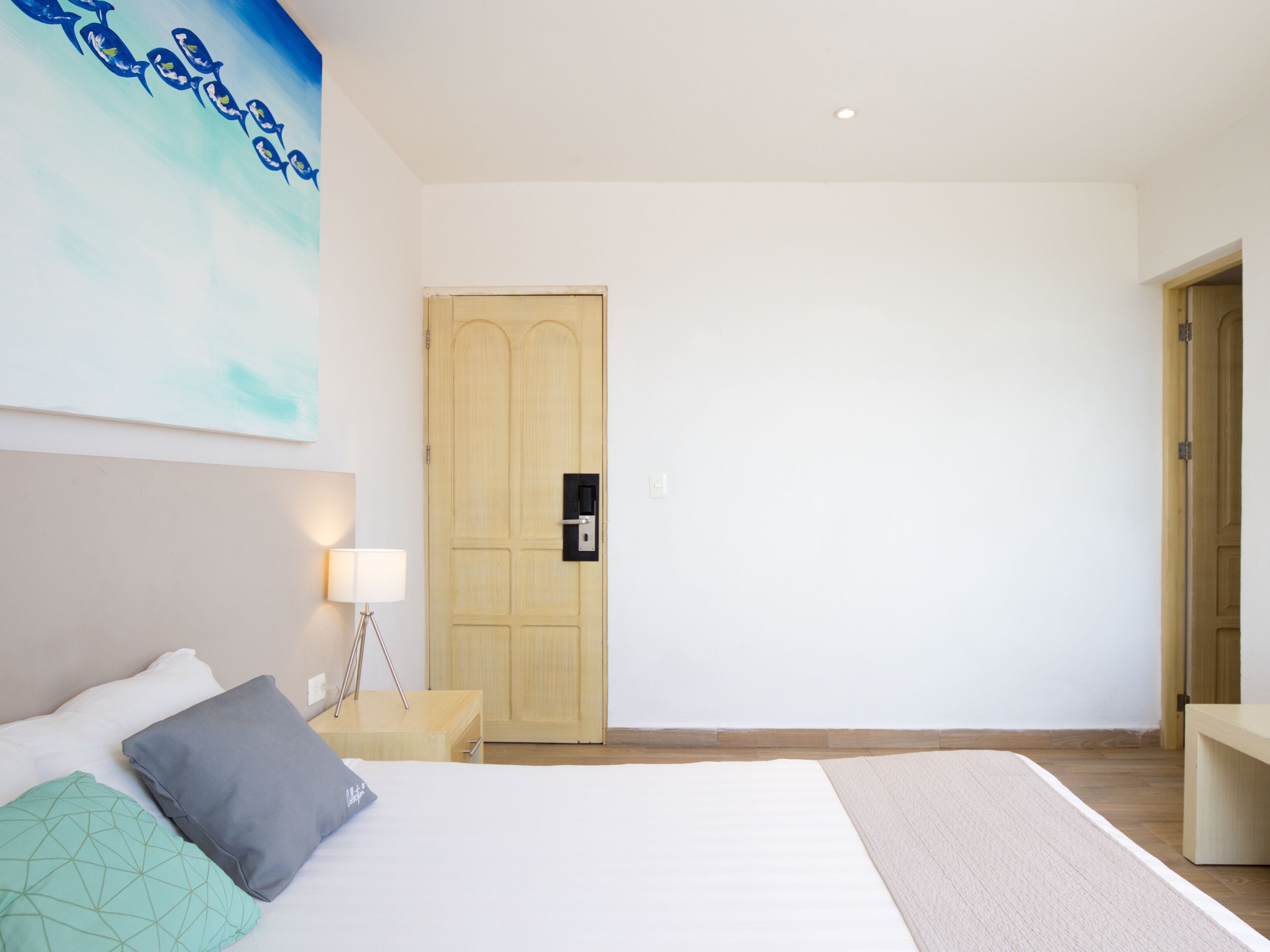 A bedroom with a bed, bedside table, lamp, and a wooden door.