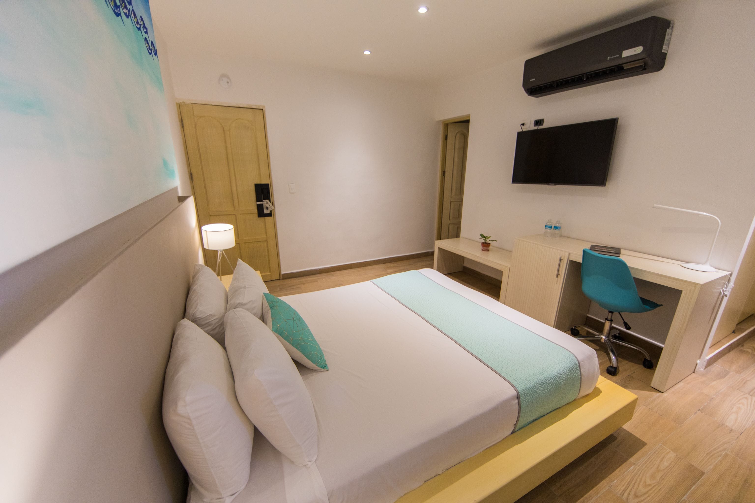 Ett hotellrum med en säng, ett skrivbord, en stol, en TV och en luftkonditioneringsanläggning.