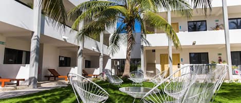 A courtyard with white metal chairs, a palm tree, and a building with balconies.
