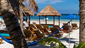 A beach with palm trees, thatched-roof huts, and wooden lounge chairs. - Hotel Ojo de Agua (Puerto Morelos)