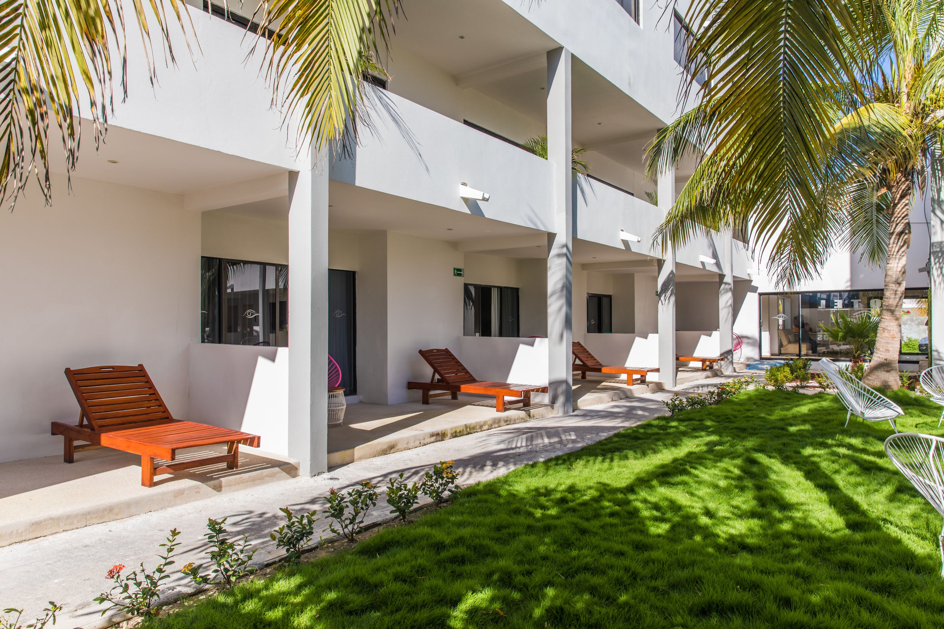 A modern building with a covered outdoor area, multiple lounge chairs, and a well-maintained lawn.