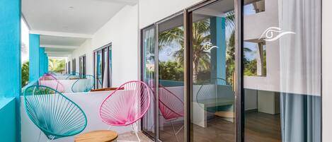 A balcony with colorful chairs and a small table, large sliding glass doors, and a view of greenery.