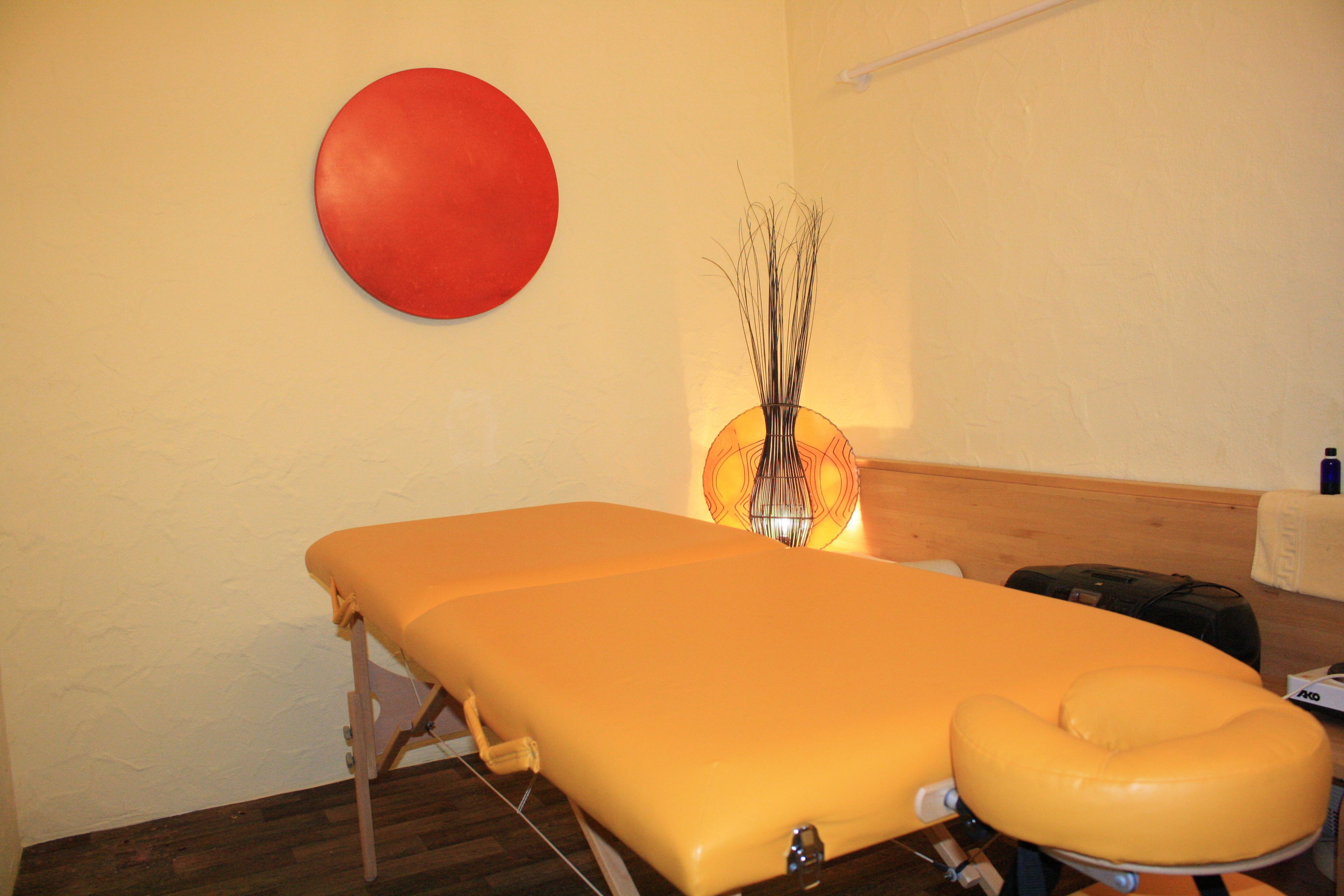 Un consultorio médico con una camilla, un objeto circular rojo en la pared y un jarrón decorativo con ramas.