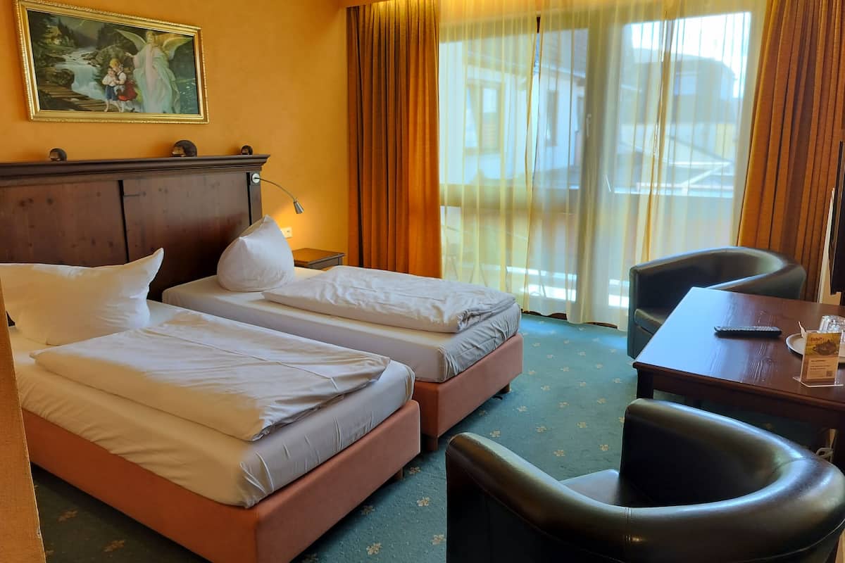 Camera d'albergo con due letti, una scrivania, una sedia, una lampada e un quadro appeso al muro.