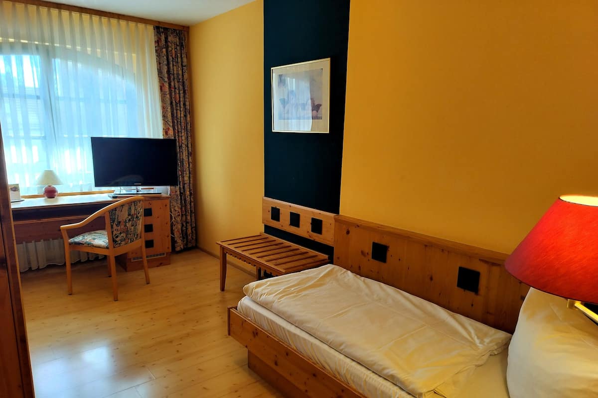 Una stanza con un letto, una scrivania con una sedia, una TV e una lampada.