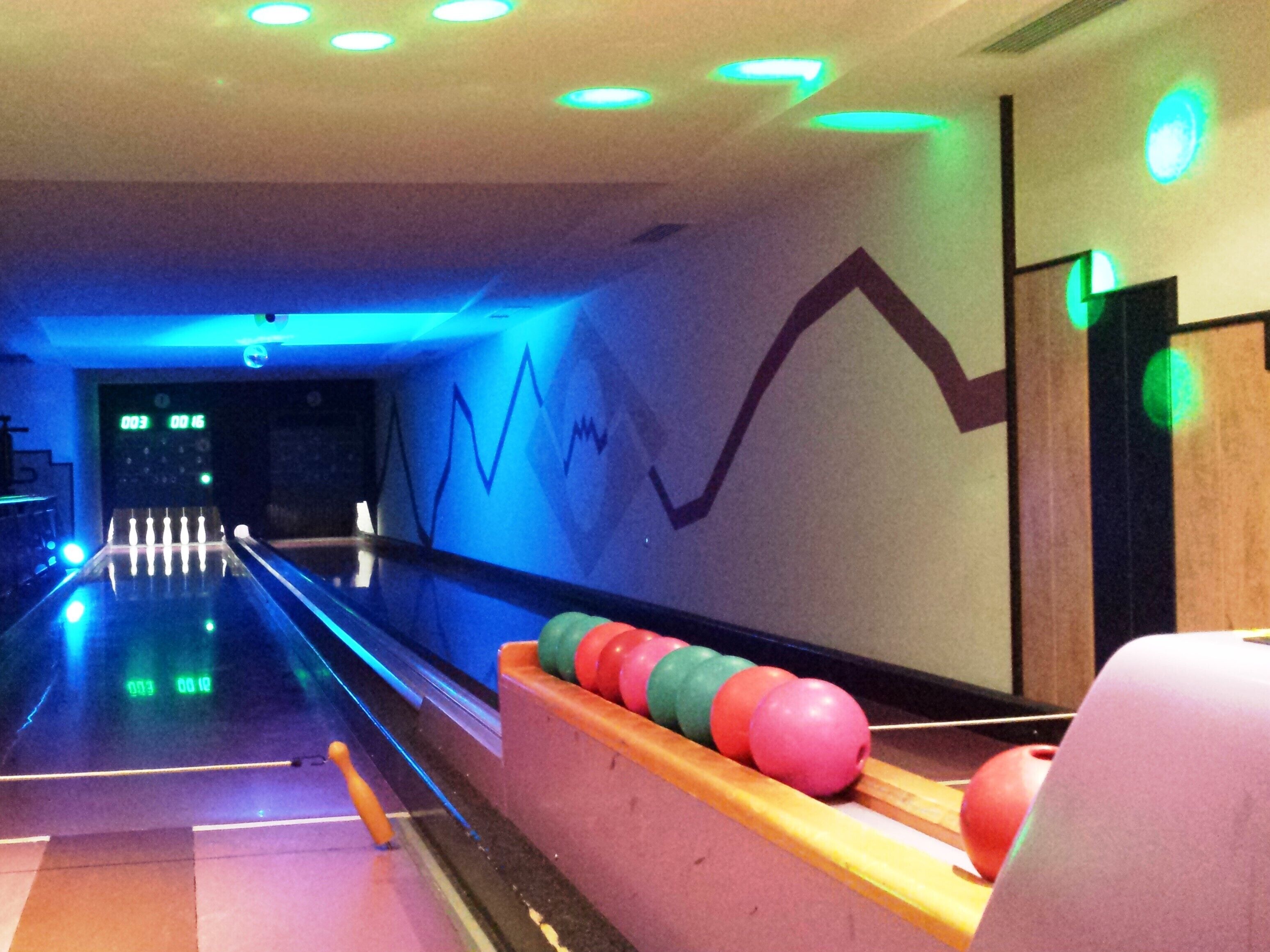 Eine Kegelbahn mit einer Holzspur, einem Automat und einer Reihe bunter Bowlingkugeln.