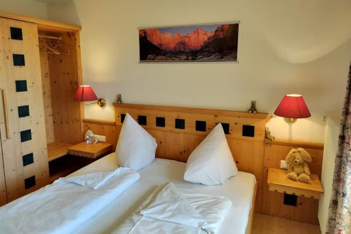 Camera da letto con testiera in legno, due lampade ai comodini, un letto con lenzuola bianche, un armadio in legno e un quadro appeso al muro.