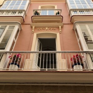A building facade with a central entrance, balconies with railings, and potted plants.