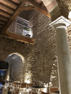 Un intérieur en pierre avec un plafond haut, des poutres en bois et un balcon agrémenté de plantes en pot.