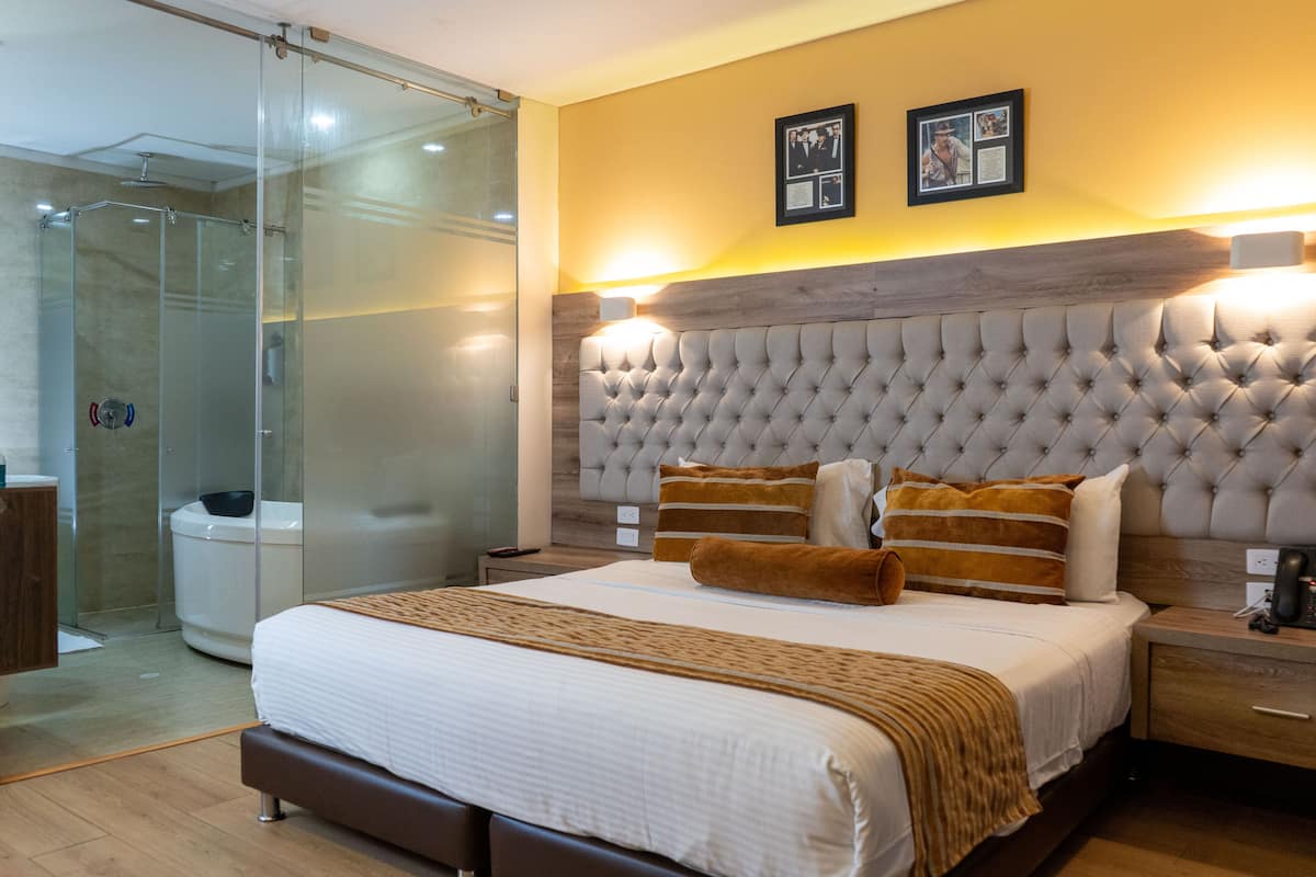 Quarto de hotel moderno com uma cama grande, box de vidro para o chuveiro e cabeceira de madeira.
