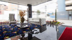 A modern lobby with a reflective floor, a white sofa, a tufted chair, and a vase with dried plants. - De Película Apartasuites (Bogotá)