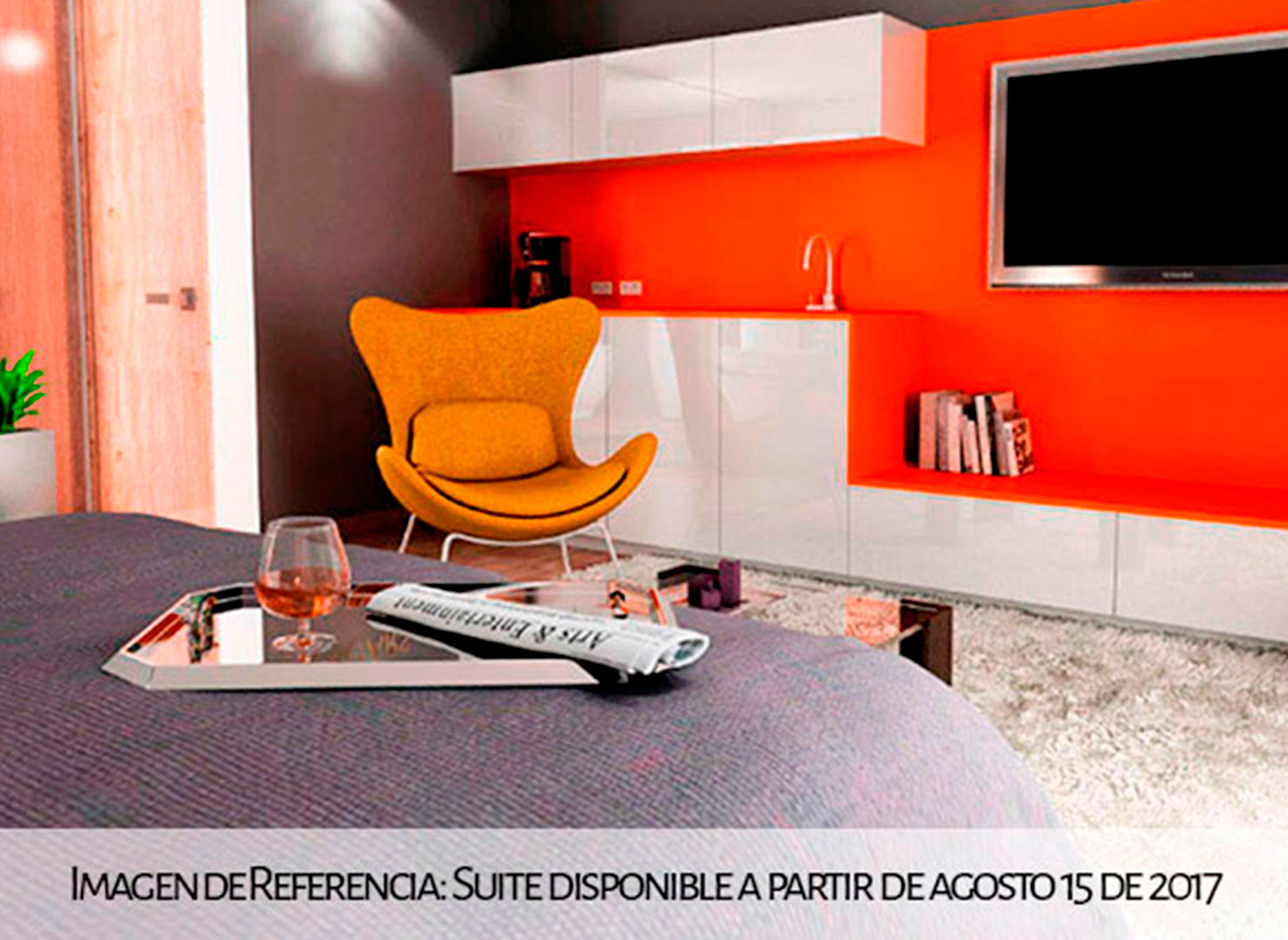 Een moderne hotelkamer met een rode accentmuur, een comfortabele oranje fauteuil, een flatscreen televisie en een tijdschrift op het bed.