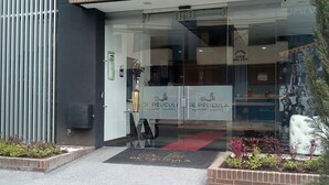A modern building entrance with a glass door, a black metal fence, and a doormat with the hotel name. - De Película Apartasuites (Bogotá)
