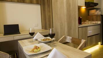 Un espace repas moderne avec une table en bois, deux assiettes de nourriture, deux verres de vin rouge et un ordinateur portable posé sur la table.