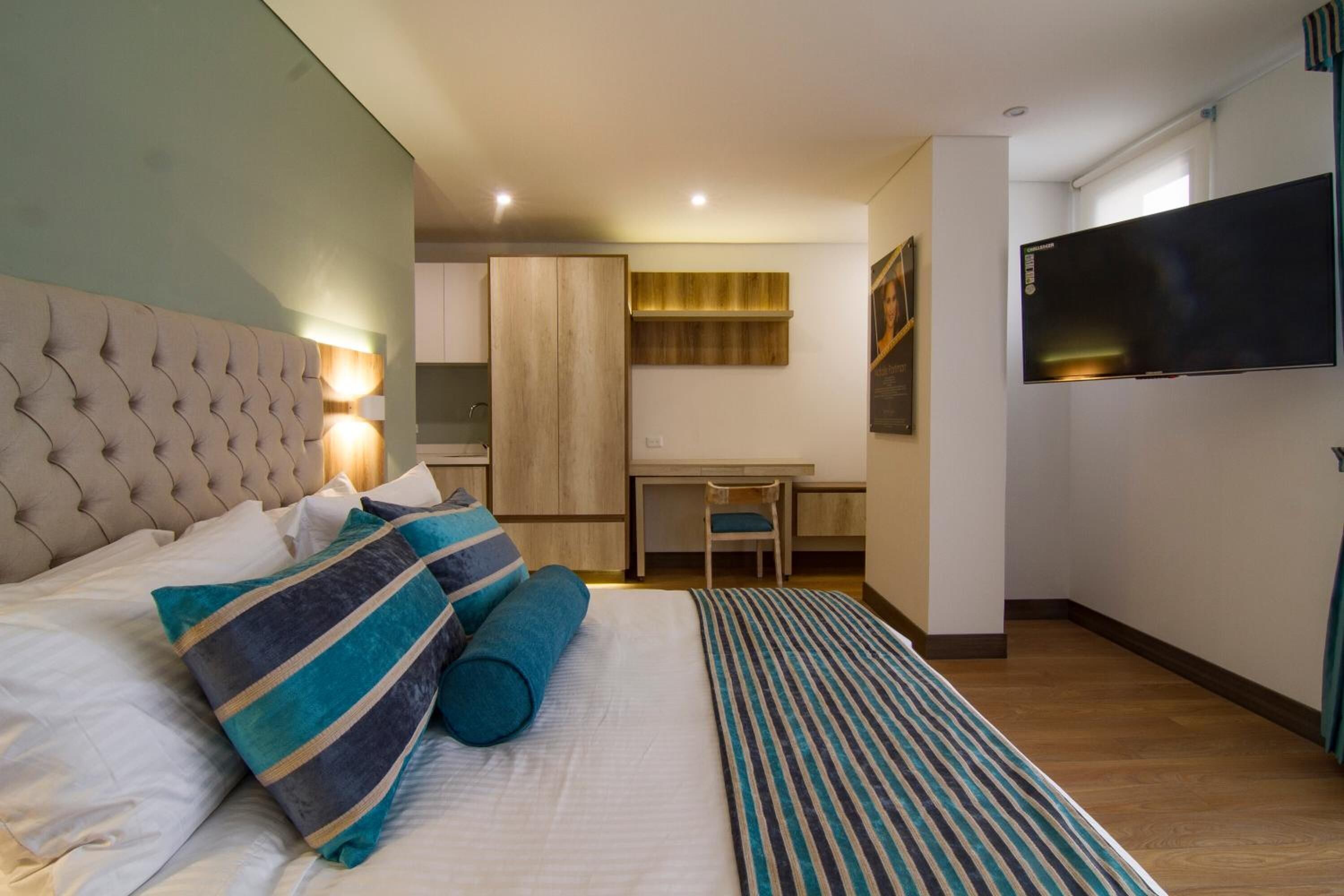 A hotel room with a bed, a desk, a chair, and a television.