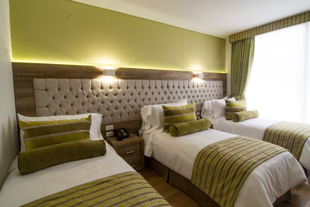 Quarto de hotel com três camas, cada uma com roupa de cama listrada em verde, cabeceira de madeira e telefone ao lado da cama.