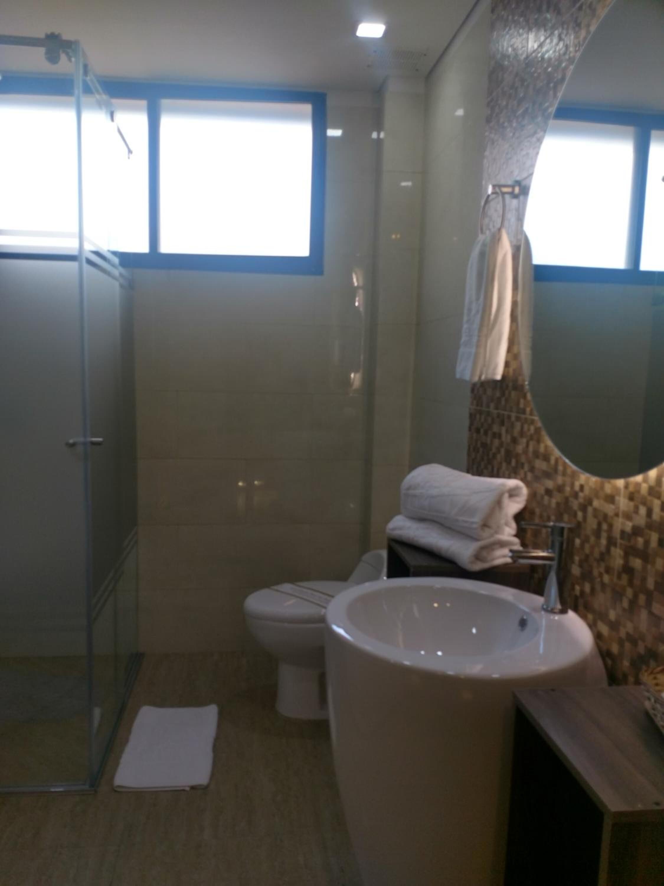 A bathroom with a glass shower enclosure, a toilet, a large freestanding bathtub, and a mirror with a patterned wall.