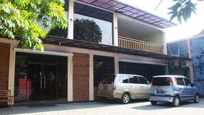 A building with a glass entrance, a balcony, and parked cars. - RedDoorz Plus near Stadion Mandala Krida (Yogyakarta)