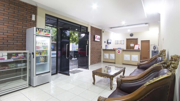 A reception area with a refrigerator, a glass display case, a reception desk, and a seating area with a coffee table and cushioned chairs. - RedDoorz Plus near Stadion Mandala Krida (Yogyakarta)