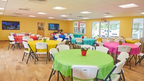 A brightly lit conference room with multiple tables and chairs, yellow walls, and large windows allowing natural light. - Chincoteague Island KOA (Chincoteague)
