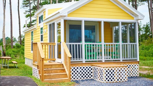 A yellow cabin with a wooden deck, white railings, and a covered porch area. - Chincoteague Island KOA (Chincoteague)