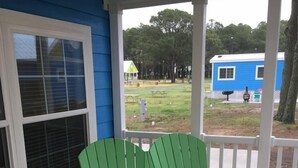 A green Adirondack chair with a geometric-patterned pillow and a red geometric-patterned pillow on a wooden deck with a blue house in the background. - Chincoteague Island KOA (Chincoteague)