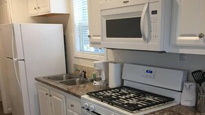 A kitchen with white cabinets, a stove, a microwave, and a refrigerator. - Chincoteague Island KOA (Chincoteague)