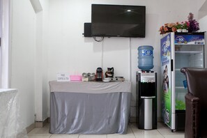 A small office with a desk, a coffee machine, a water dispenser, a refrigerator, and a television mounted on the wall. - RedDoorz Plus near Sukajadi 2 (Bandung)