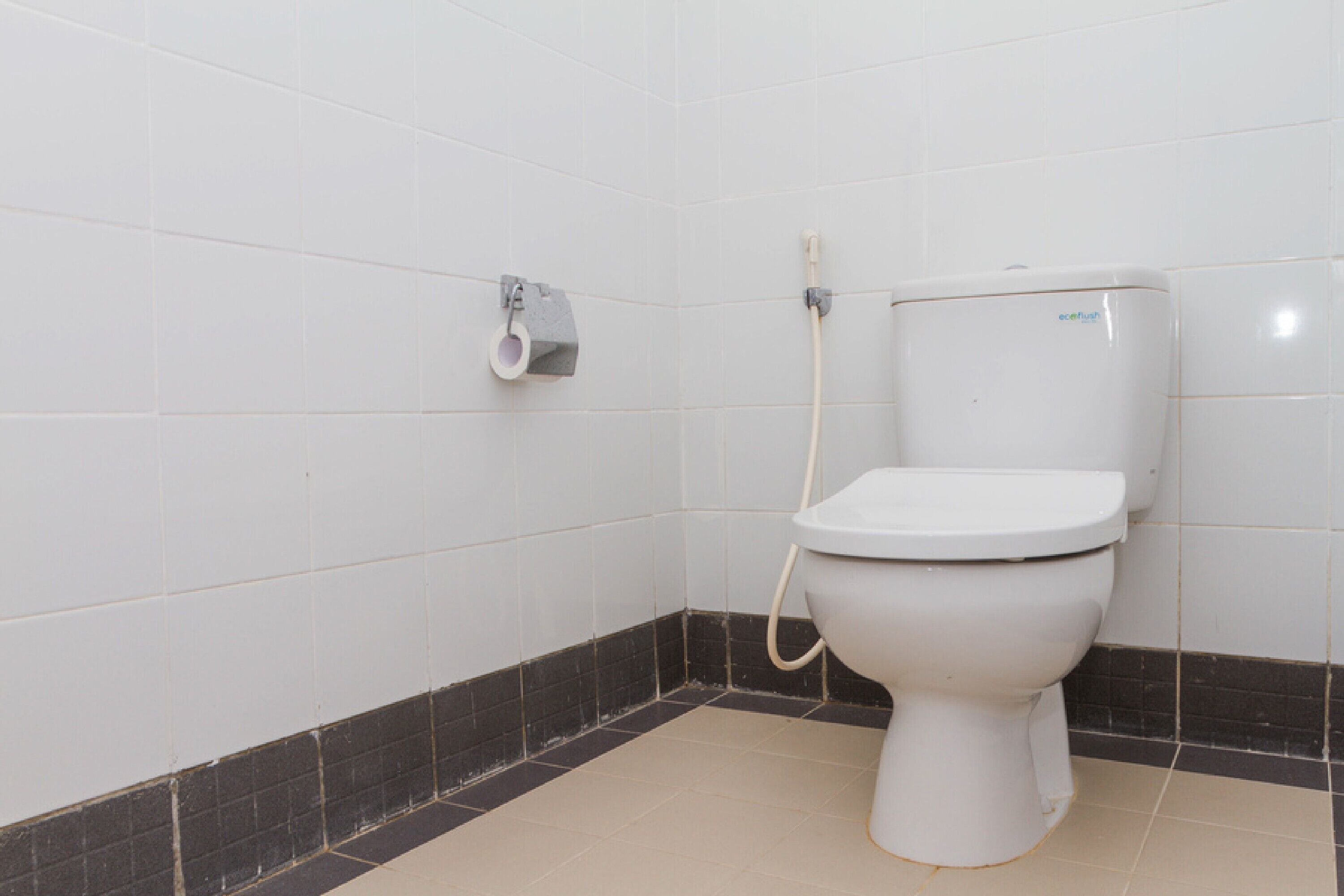 A standard bathroom with a toilet, a paper towel dispenser, and a toilet paper roll.