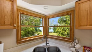 A kitchen with a double sink, wooden cabinets, and a window with a view of trees. - Lakeview on the Lake (Harborcreek)