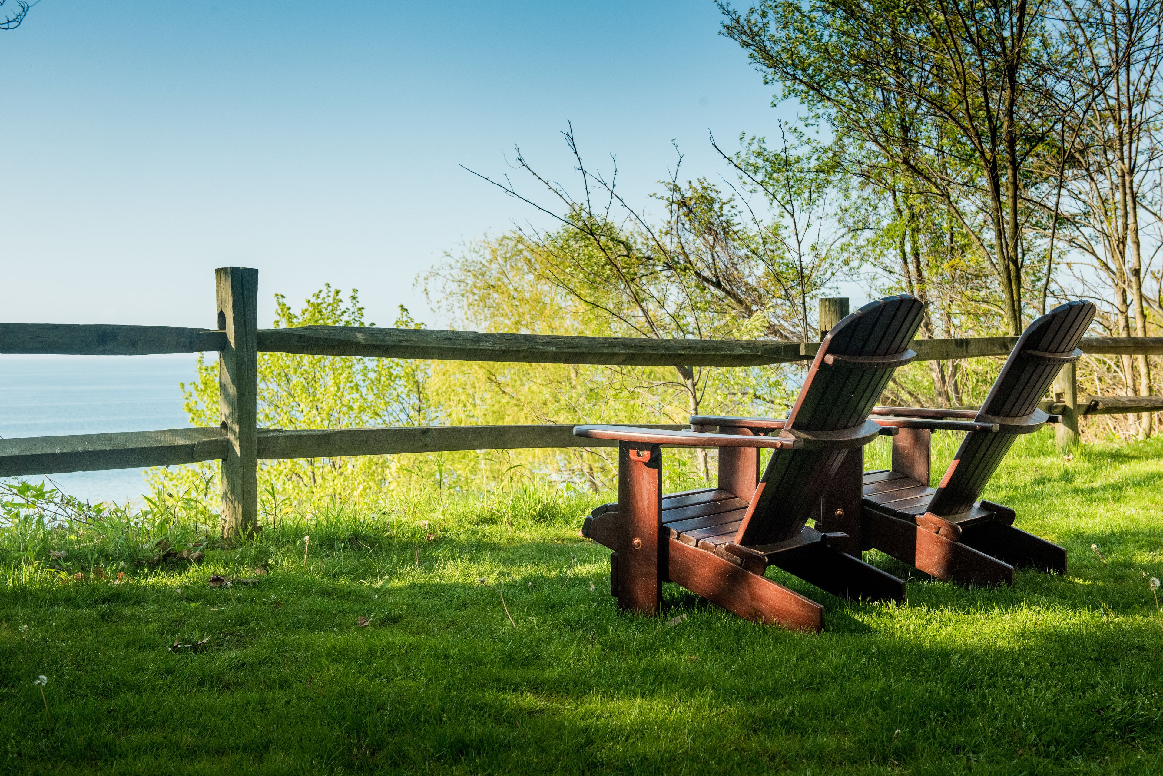 A wooden deck with two Adirondack chairs facing a body of water, surrounded by lush greenery.