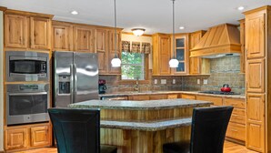 A modern kitchen with wooden cabinets, stainless steel appliances, a granite countertop island, and pendant lighting. - Lakeview on the Lake (Harborcreek)