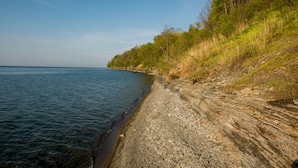 A coastal landscape with a rocky shoreline and dense vegetation on a hillside. - Lakeview on the Lake (Harborcreek)