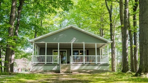 A small, single-story cabin with a porch, surrounded by trees. - Lakeview on the Lake (Harborcreek)