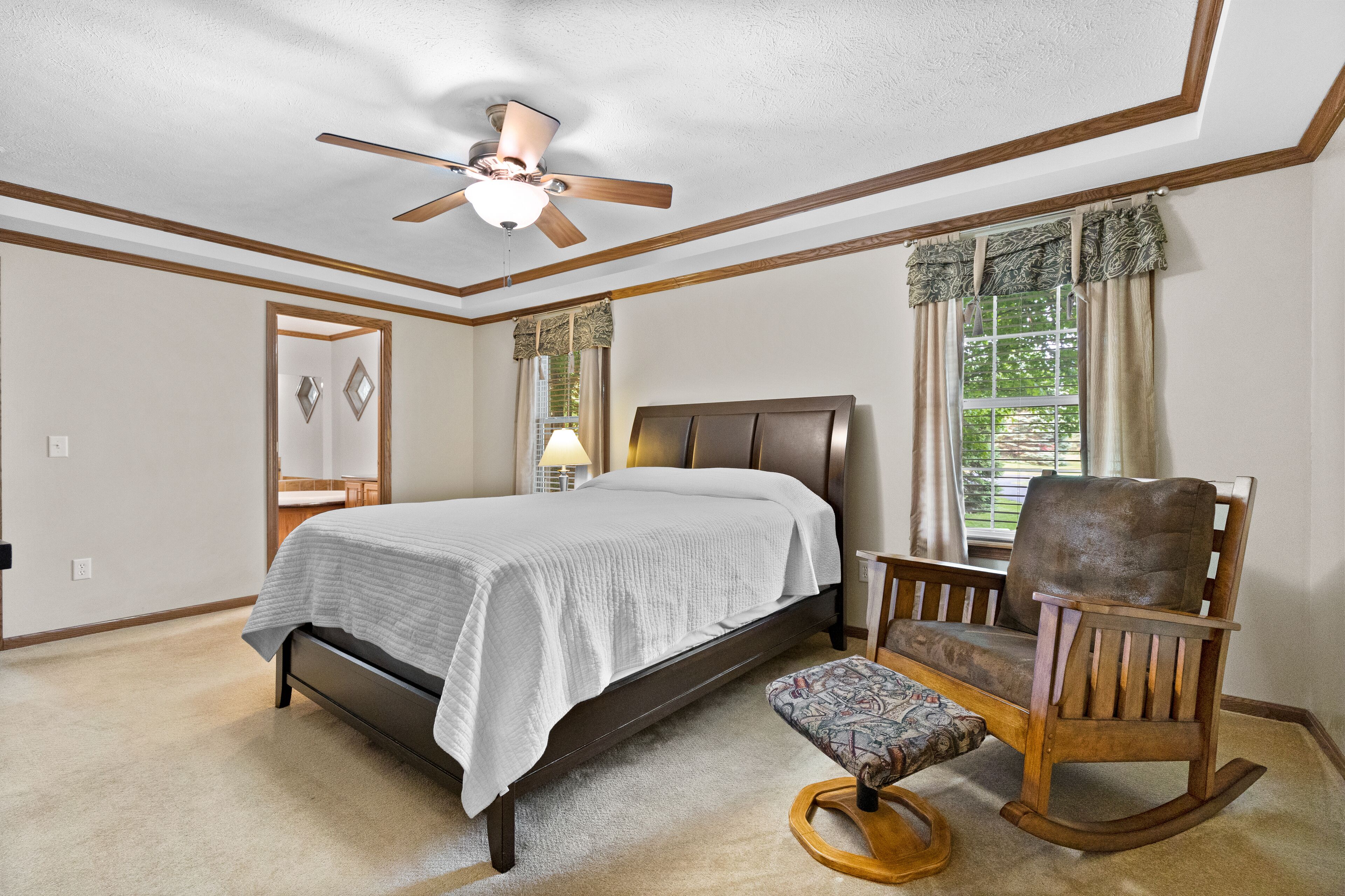 Ein Schlafzimmer mit einem Bett, einem Schaukelstuhl, einem kleinen Tisch, einer Lampe und einem Deckenventilator.