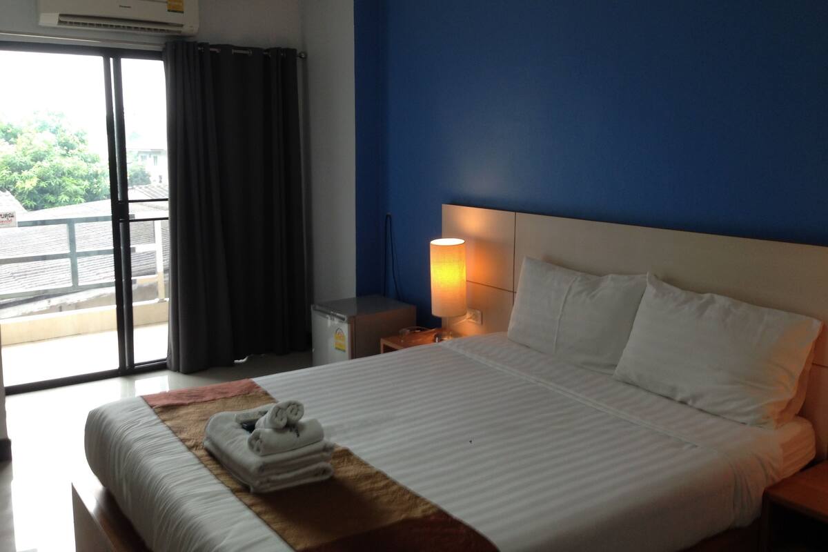 A hotel room with a bed, a nightstand, a lamp, and an air conditioning unit.