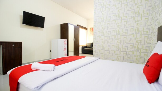 A hotel room with a bed, a TV mounted on the wall, a wardrobe, and a patterned wall. - RedDoorz @ Swakarya Kaliurang (Depok)