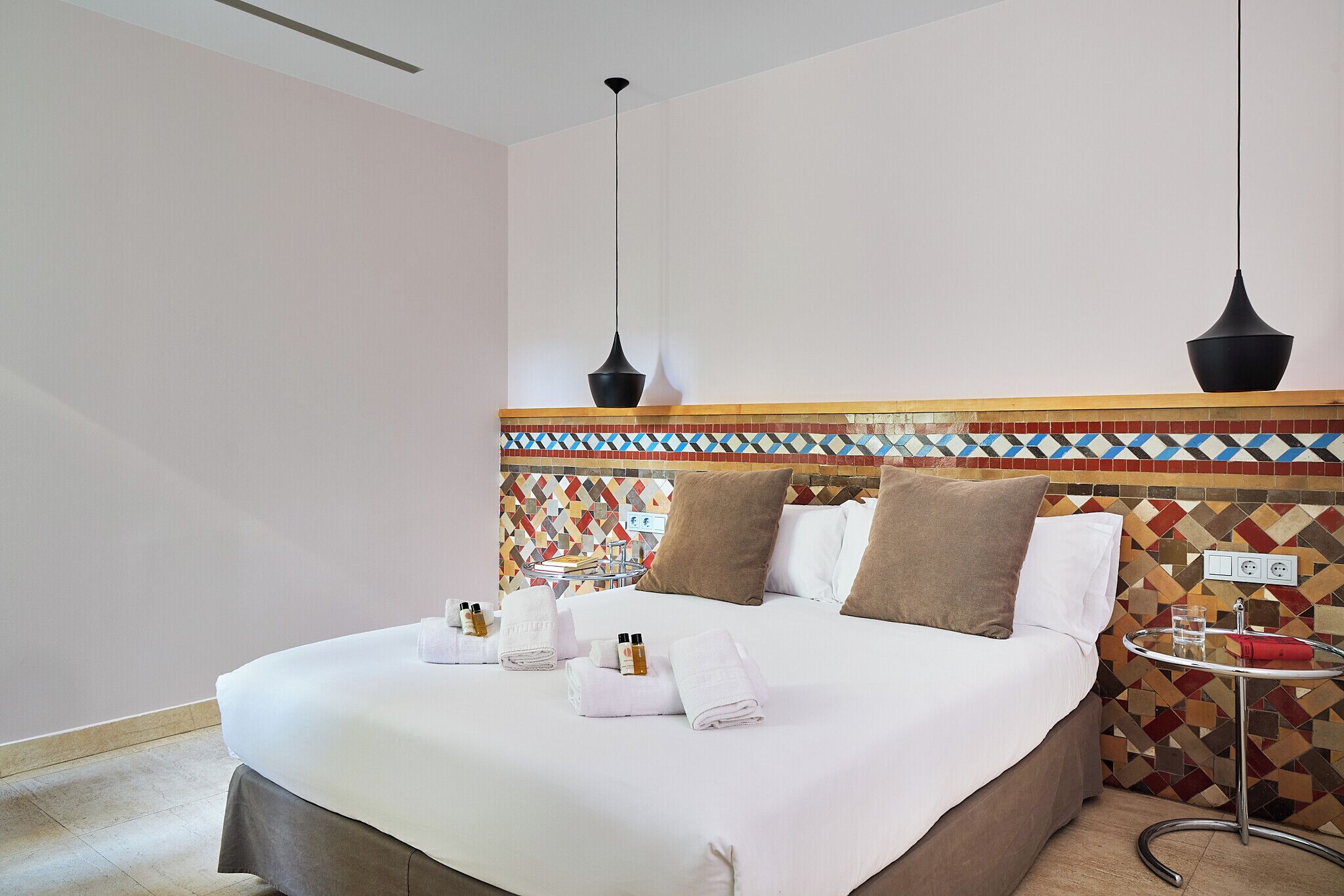 A neatly made bed with towels and toiletries, a small round table with a glass, and a patterned wall.