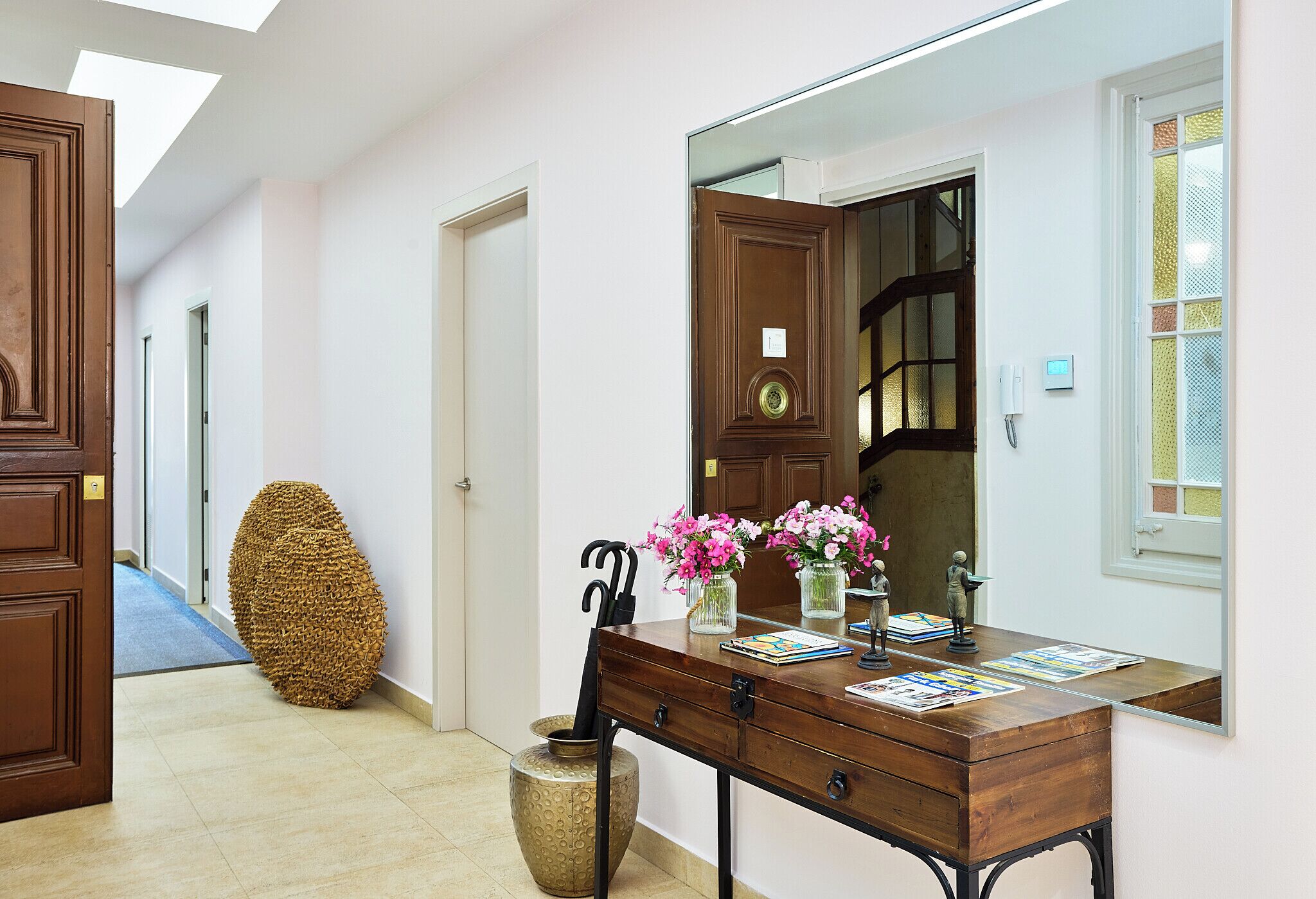 Un pasillo con un escritorio de madera, un espejo grande y un jarrón decorativo con flores.