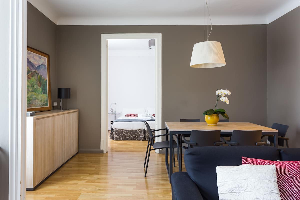 Uma sala de estar moderna com um sofá azul escuro, uma mesa de jantar de madeira e uma área de cozinha com um armário e um quadro na parede.
