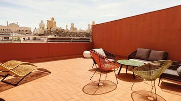 Una terraza en la azotea con sillas de mimbre, una mesa redonda y un sofá.