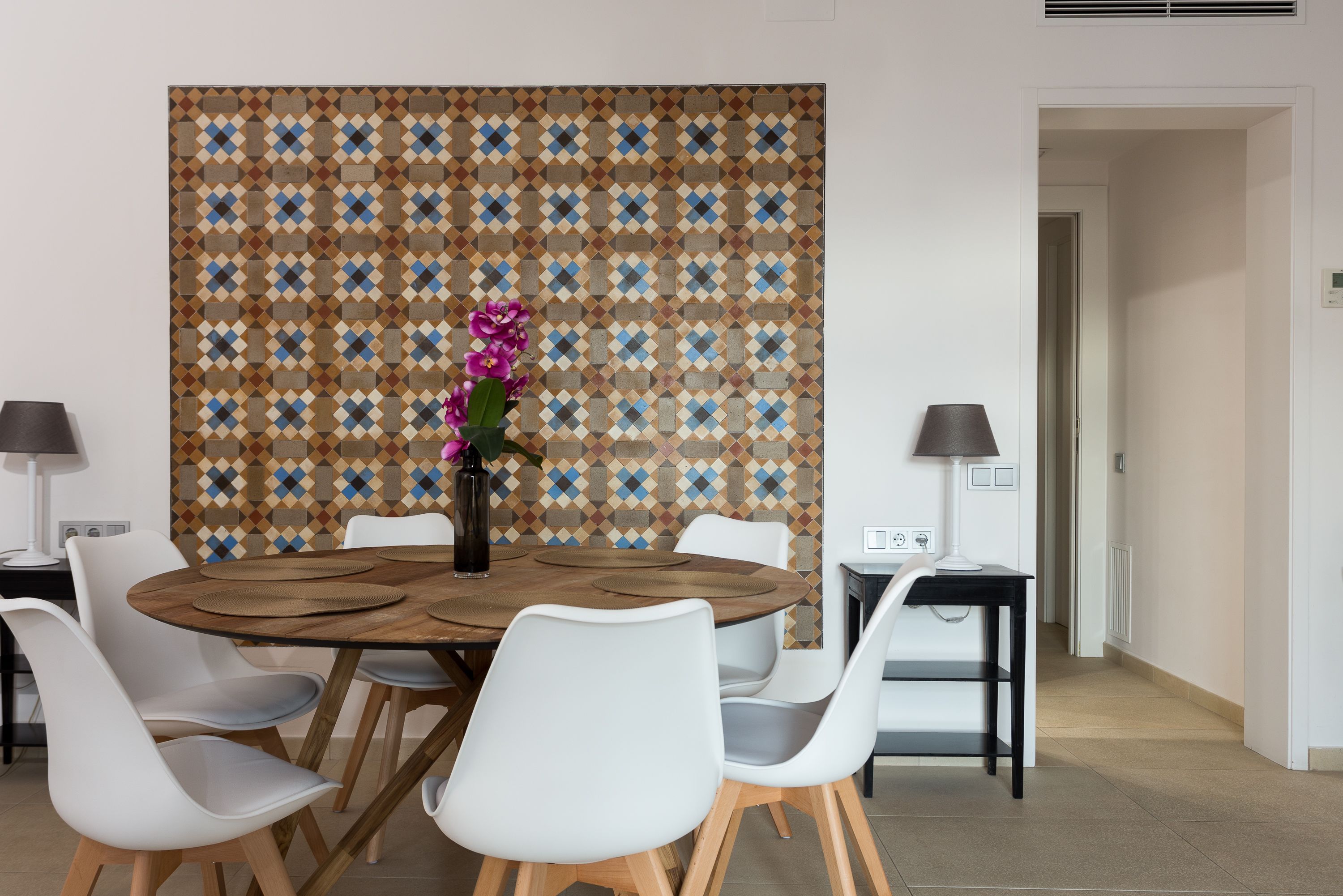 Een eetgedeelte met een ronde houten tafel, witte stoelen en een behang met patroon.