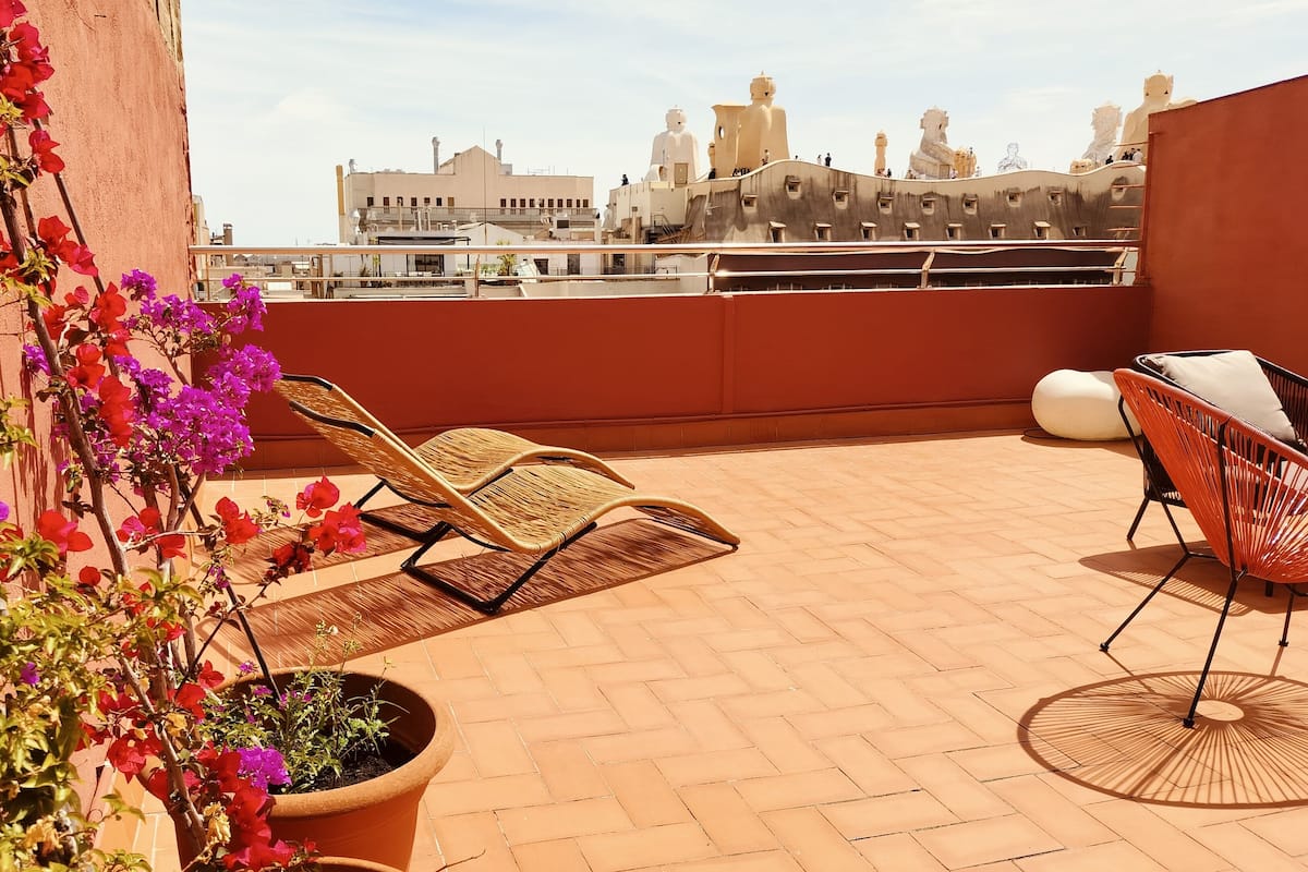 Terraço no telhado com duas poltronas de vime, um vaso de plantas e um guarda-sol decorativo.