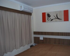 A hotel room with a bed, an air conditioning unit, a wall-mounted artwork, and a window with curtains. - Apartment L'ácqua DiRoma - Achei Férias (Caldas Novas)
