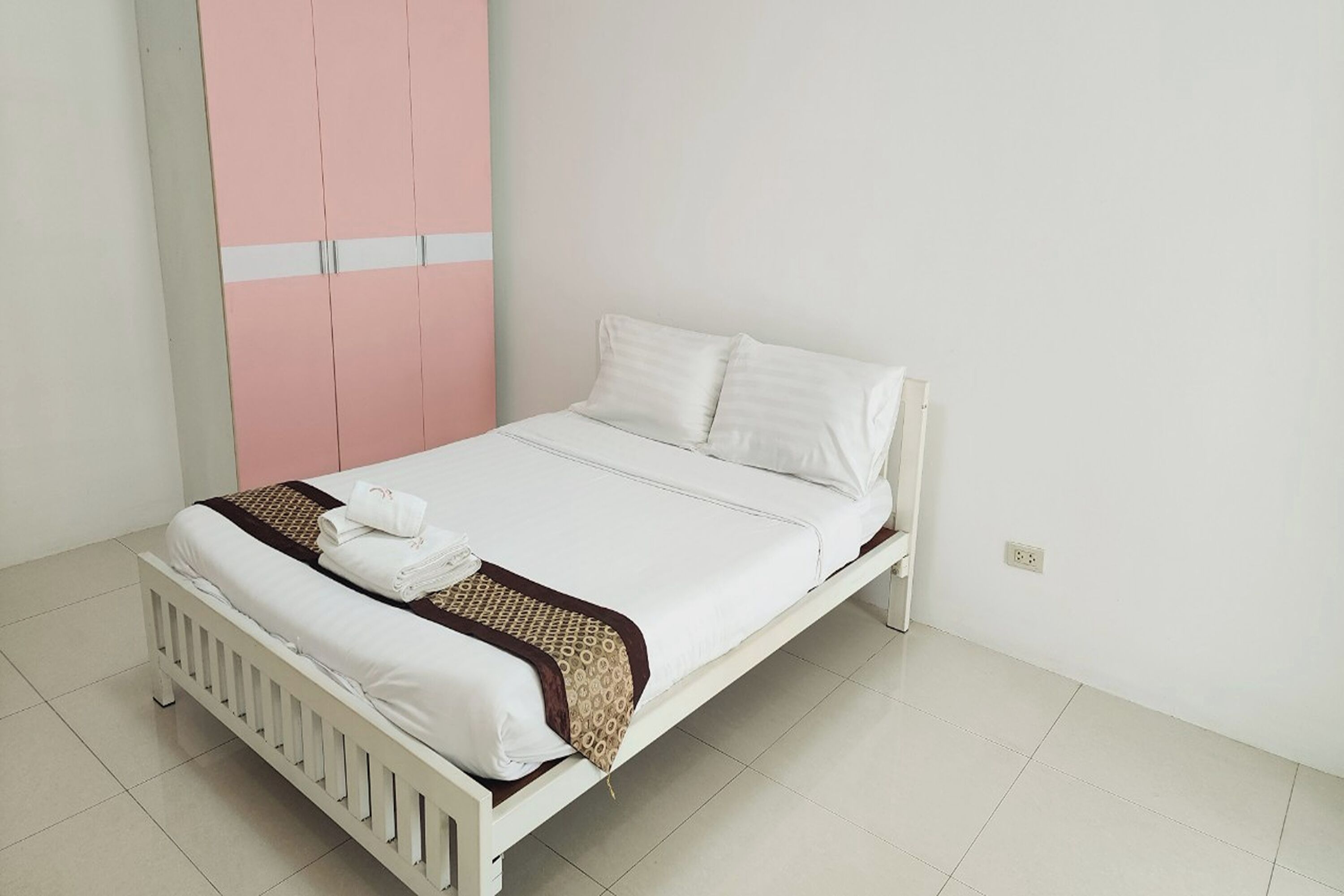 A single-bed room with a white bed, white pillows, and a brown patterned throw.